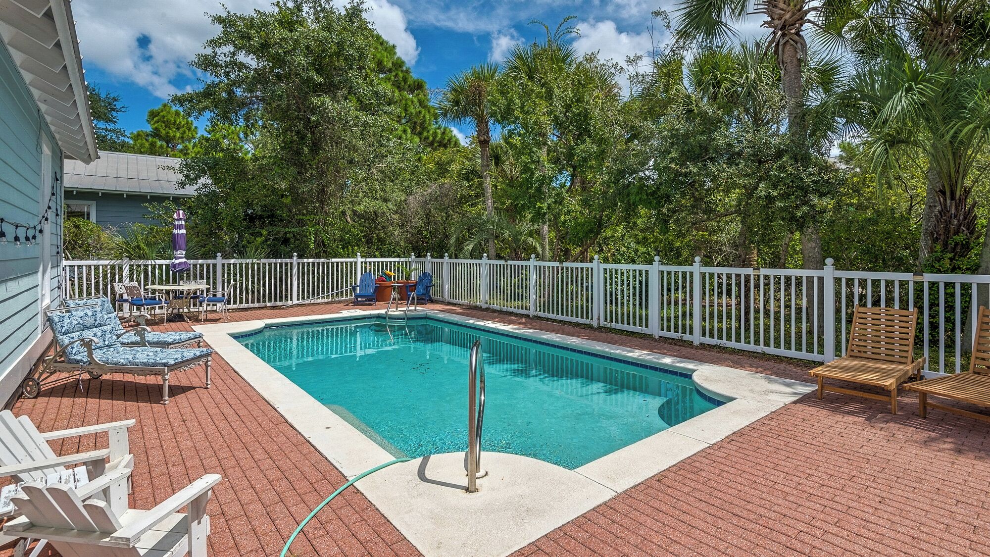 A rectangular swimming pool with a white deck and a white fence surrounding it.