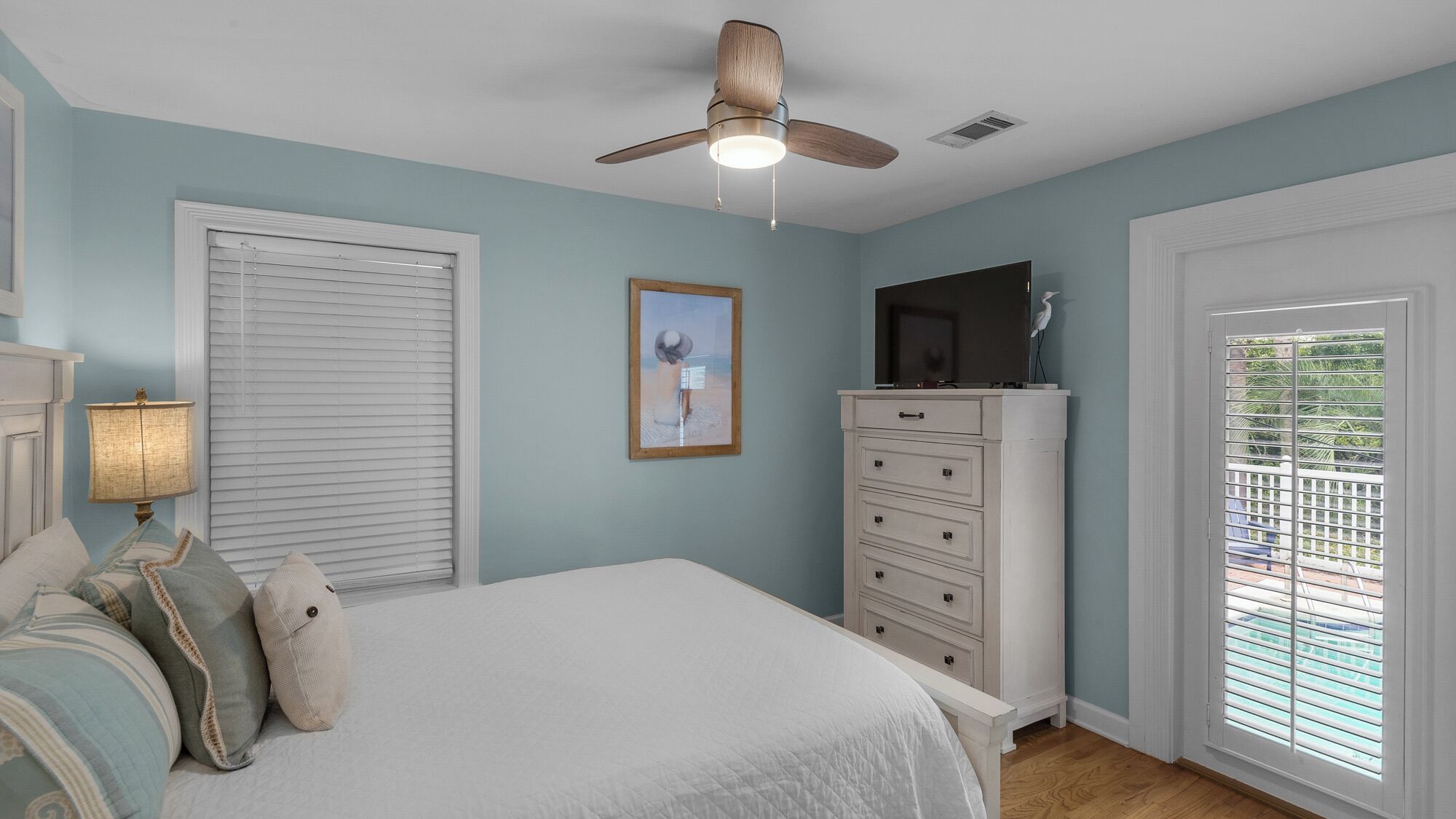 Un dormitorio con cama, cómoda, ventilador de techo, un cuadro y una ventana con persianas.