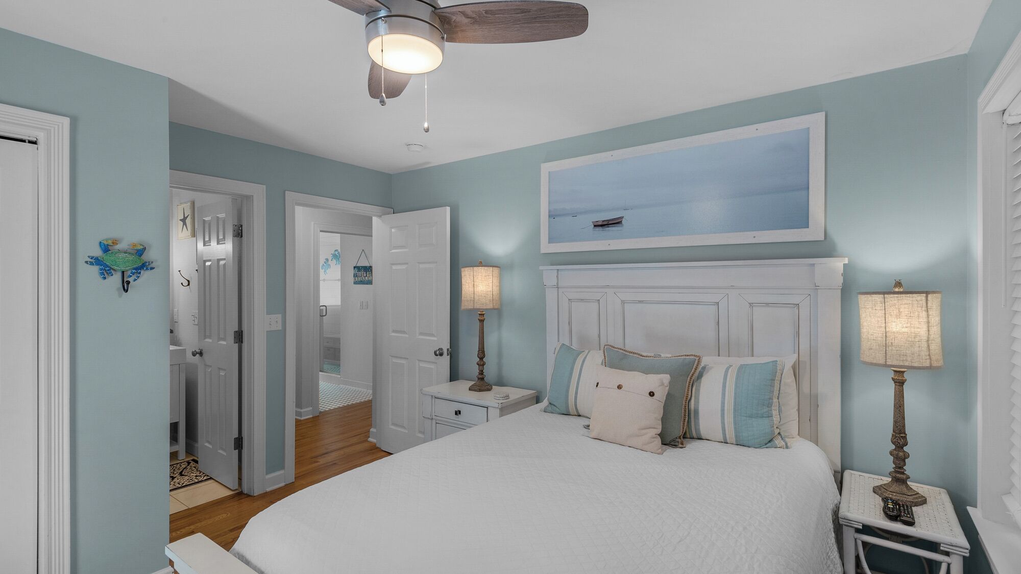 A bedroom with a large bed, a ceiling fan, and a painting of a boat on the wall.