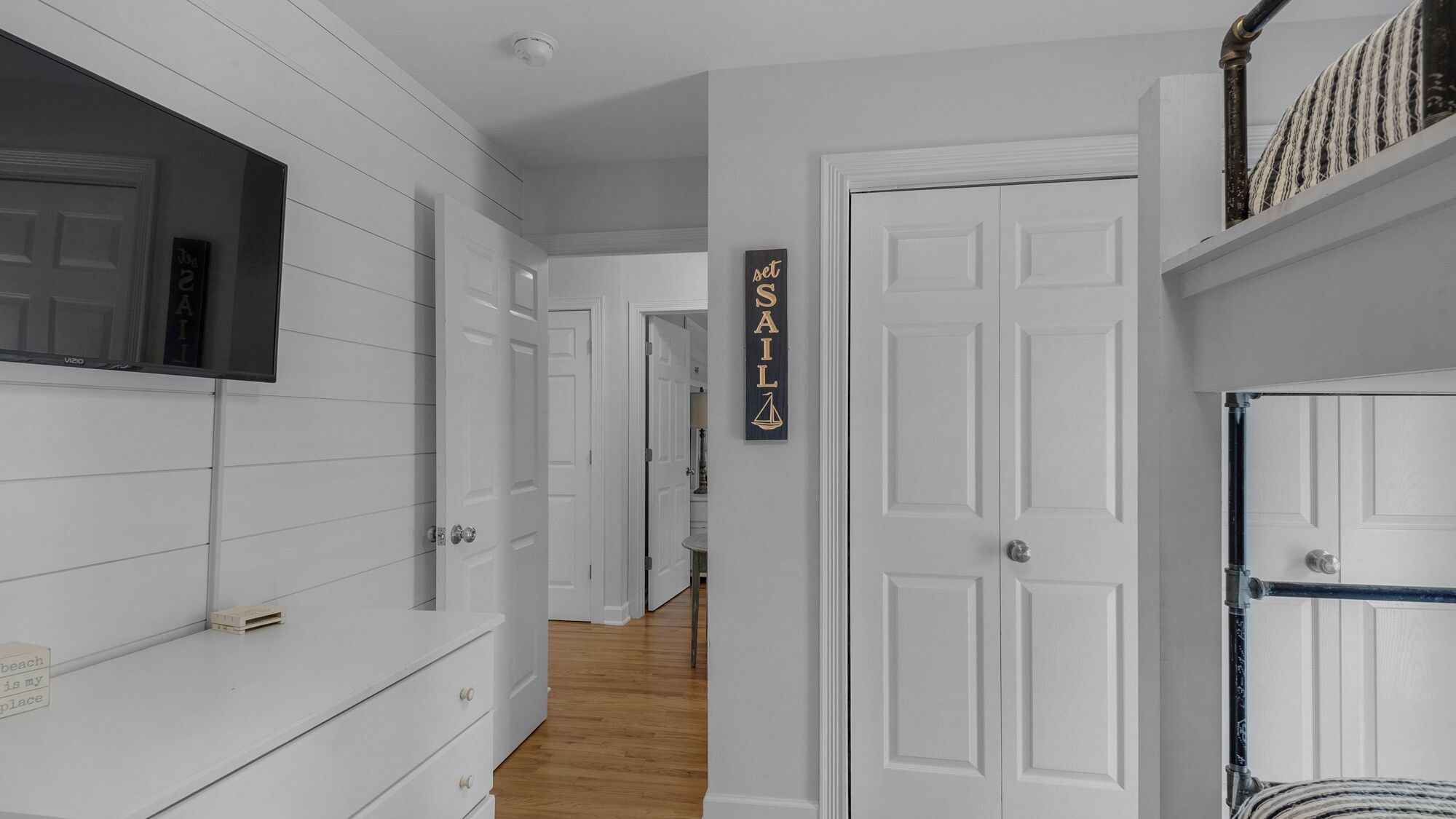 A hallway with white walls, wooden flooring, and a set sail sign on the wall.