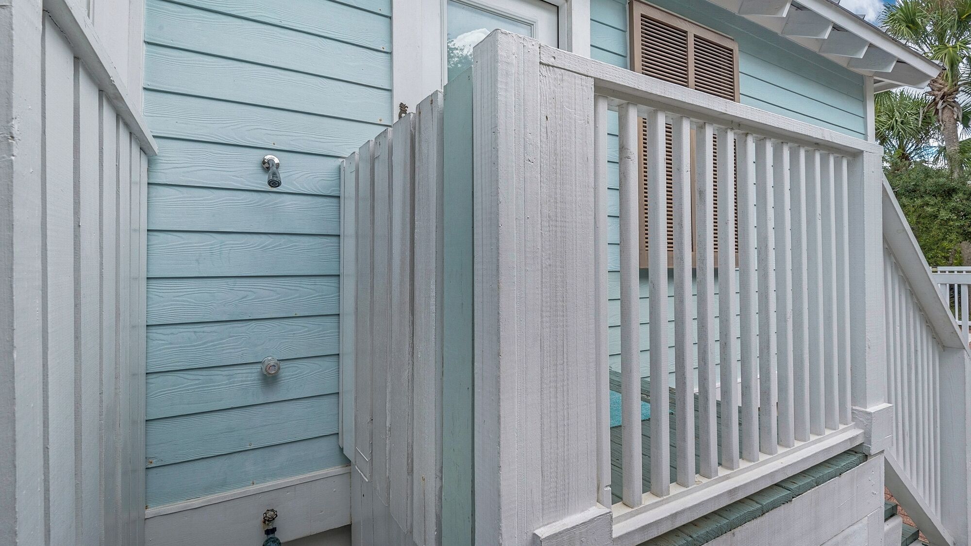 Une maison bleu clair avec une balustrade blanche sur le porche et une fenêtre avec des volets.