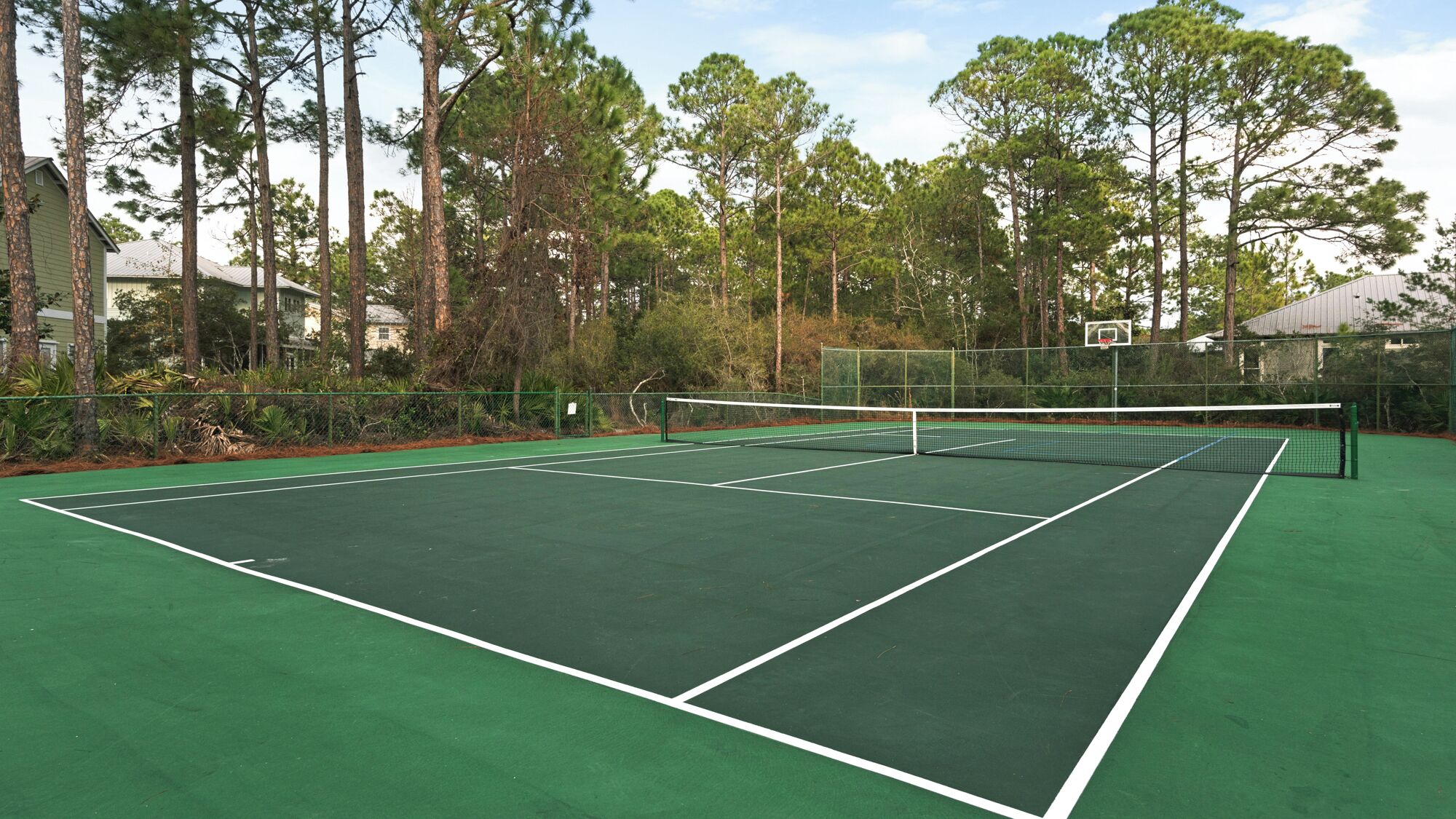 Una cancha de tenis con una red, rodeada de árboles y una valla.