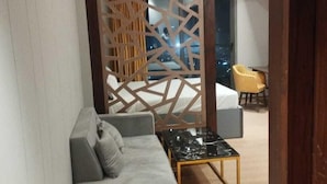 A modern living room with a grey sofa, a black coffee table, and a decorative partition. - Loft Studios Noida (Greater Noida)