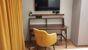 A hotel room with a wooden desk, a yellow chair, a flat-screen TV mounted on the wall, and a small potted plant. - Loft Studios Noida (Greater Noida)