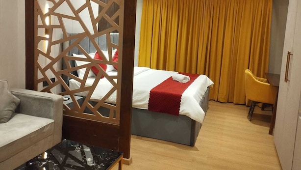 A hotel room with a bed, a desk, a chair, a sofa, and a decorative partition. - Loft Studios Noida (Greater Noida)