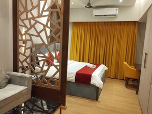 A hotel room with a bed, a desk, a chair, a sofa, and a decorative partition. - Loft Studios Noida (Greater Noida)