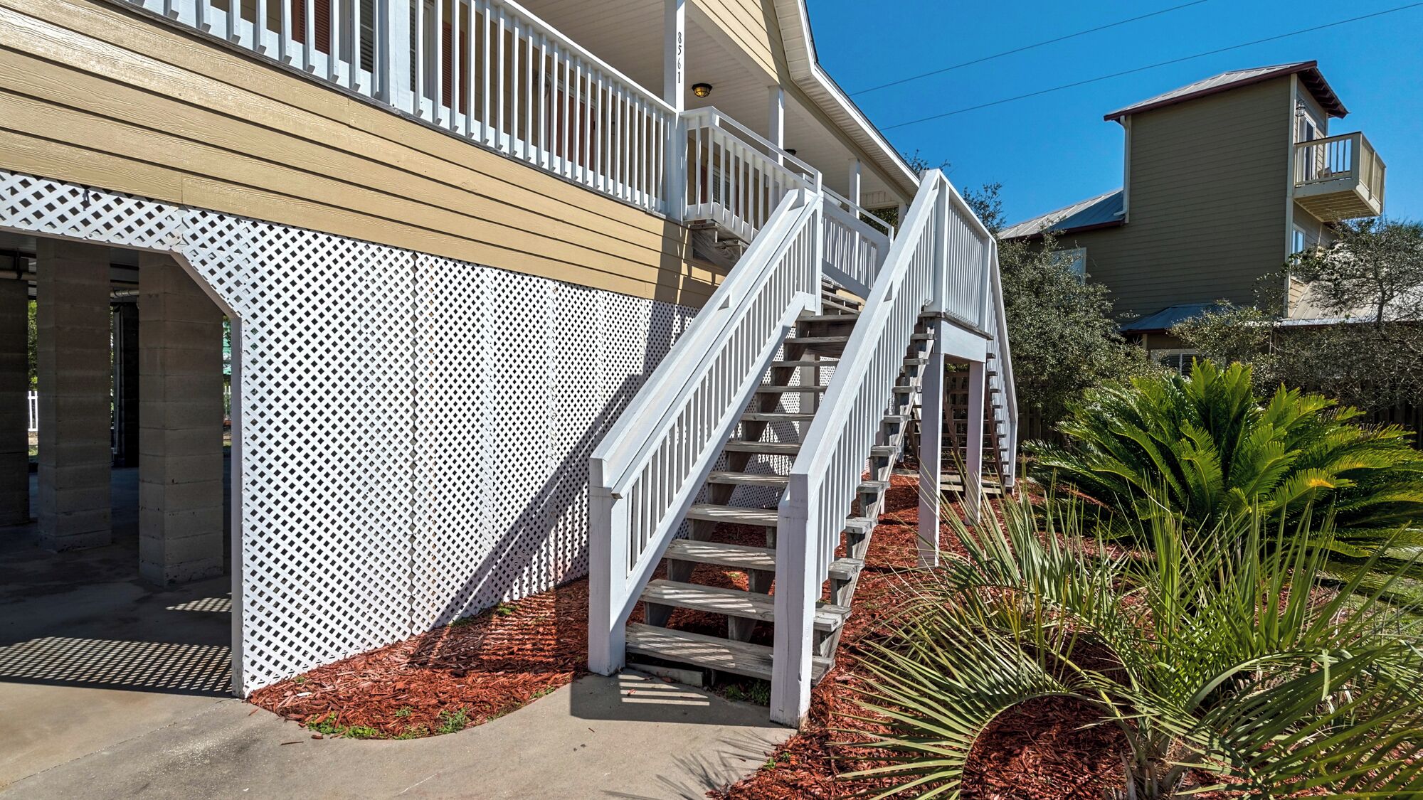 A residential building with a wooden exterior, a white fence, and a staircase leading to a balcony.