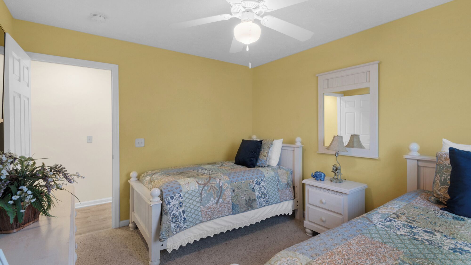 A bedroom with two beds, a ceiling fan, a nightstand, a dresser, and a mirror.