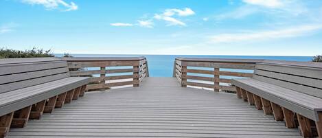 Een houten looppad dat naar een strand leidt, met bankjes aan weerszijden.