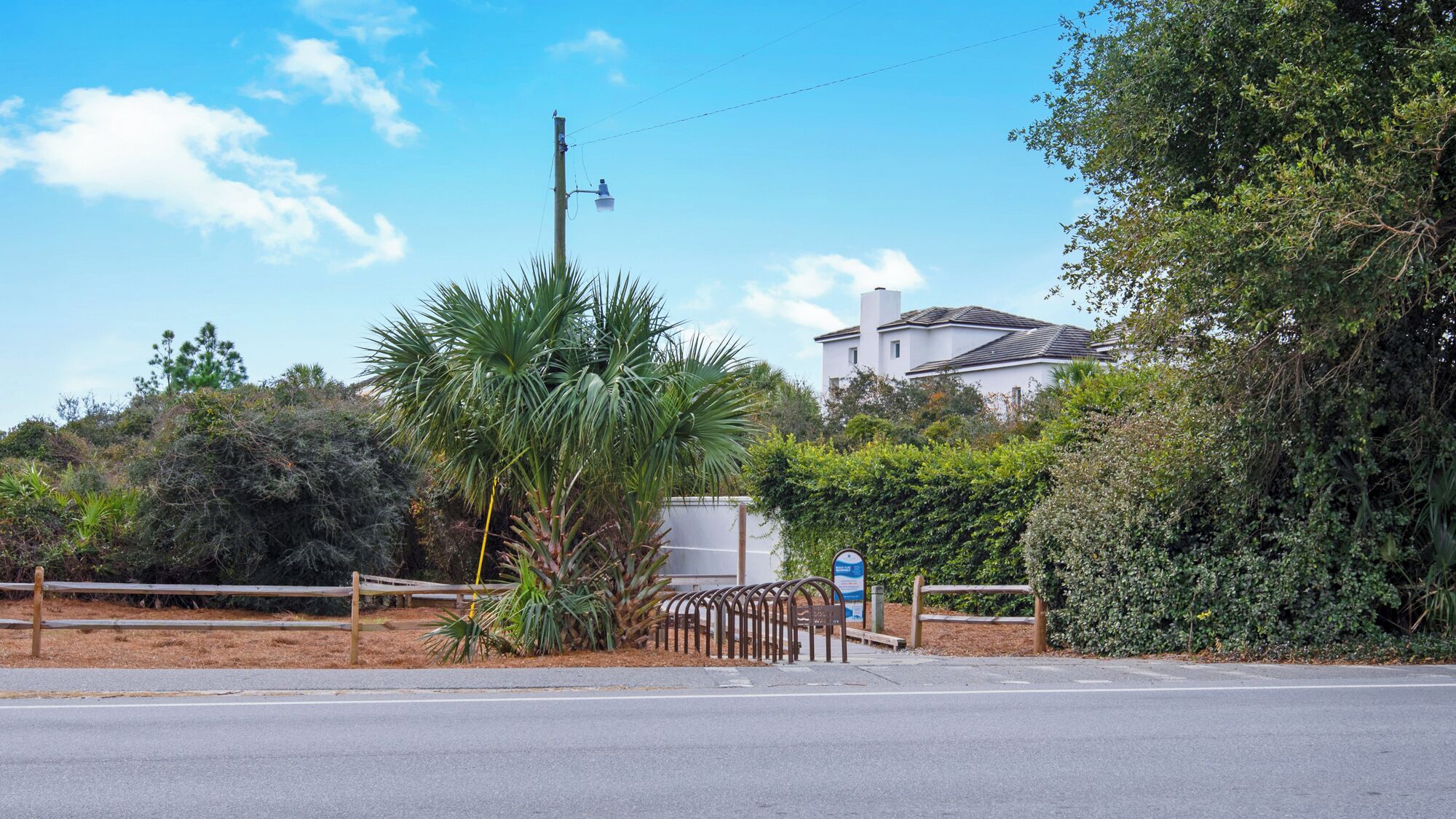 A residential area with a road, a metal fence, and a white house with a tiled roof.