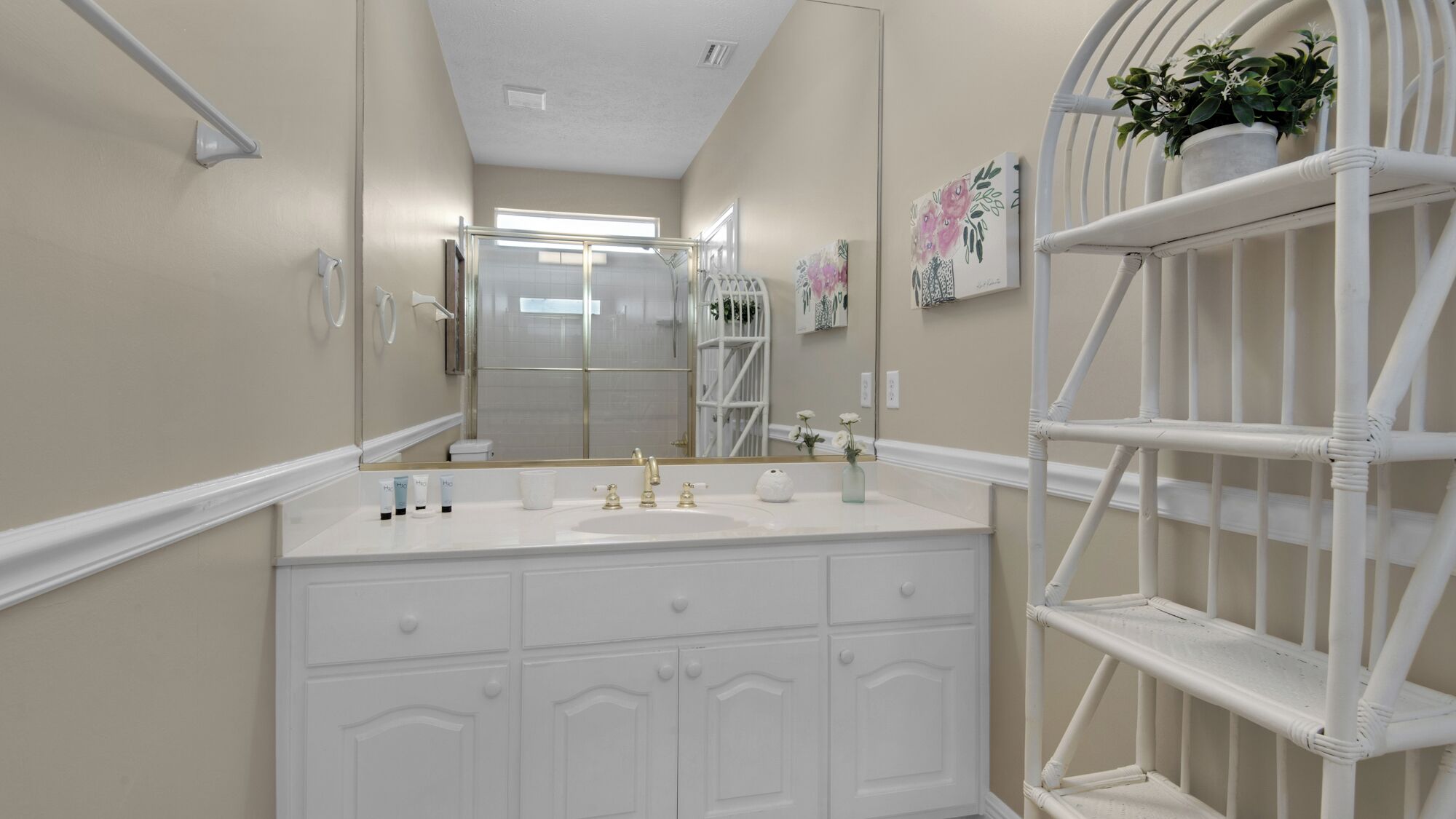 A bathroom with a white vanity, a large mirror, and a white shelving unit.