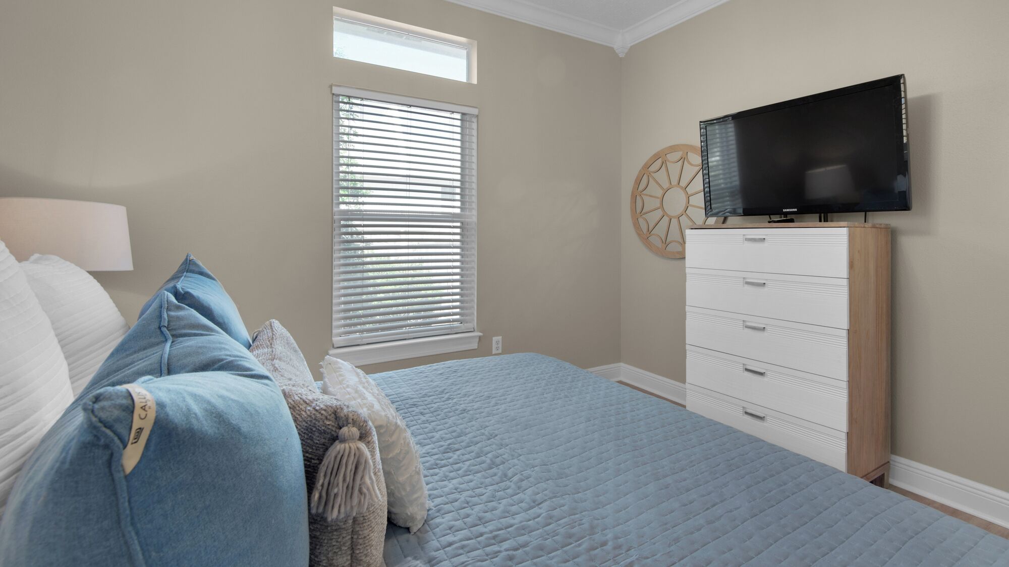 Un dormitorio con cama, cómoda, televisor y ventana con persianas.