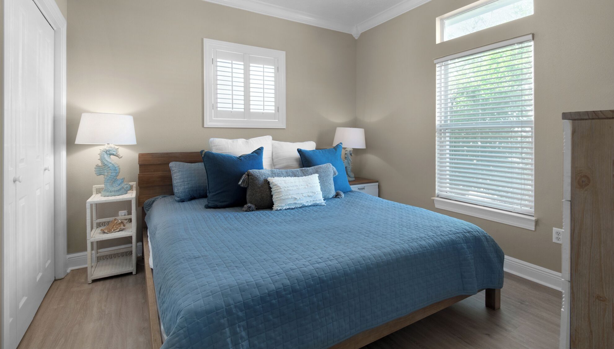 A bedroom with a large bed, two bedside tables, a nightstand, a dresser, and a window with blinds.