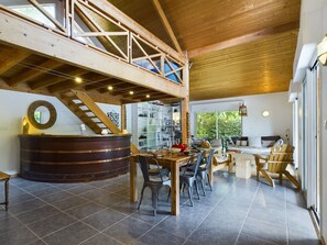 Cozy seating area with a wooden table and chairs, a large barrel-shaped object, and a staircase leading to an upper level with a view of the surrounding greenery.
