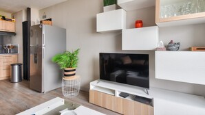 A modern kitchen with a built-in refrigerator, a TV, and a dining area with a white table. - Flat for 4, sea view and right on the water (Saint-Hilaire-de-Riez)