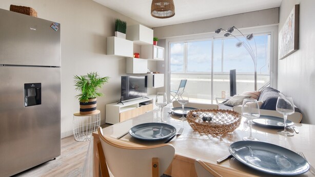 A modern kitchen with a stainless steel refrigerator, white cabinets, a dining table set with plates and glasses, and a large window offering a view. - Flat for 4, sea view and right on the water (Saint-Hilaire-de-Riez)