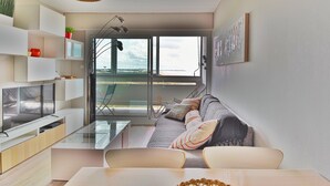 A modern living room with a sofa, TV, and glass table. There is a large window with a view of the outdoors. - Flat for 4, sea view and right on the water (Saint-Hilaire-de-Riez)
