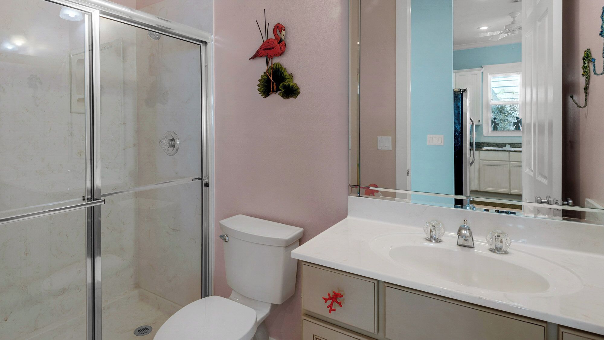 A bathroom with a glass shower enclosure, a white toilet, a vanity with a mirror, and a red decorative item on the wall.