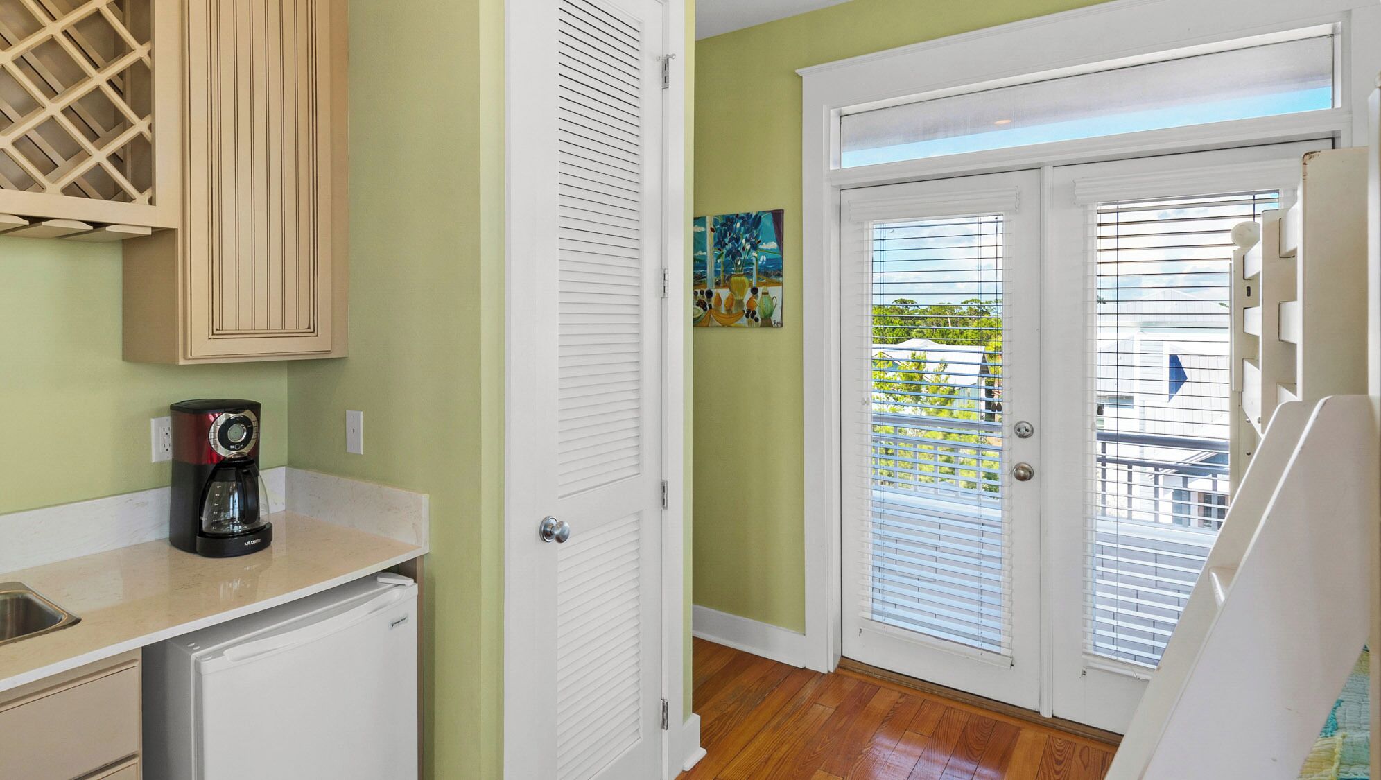 A kitchen with a coffee maker, a refrigerator, and a cabinet. There is a door with a window and a painting on the wall.