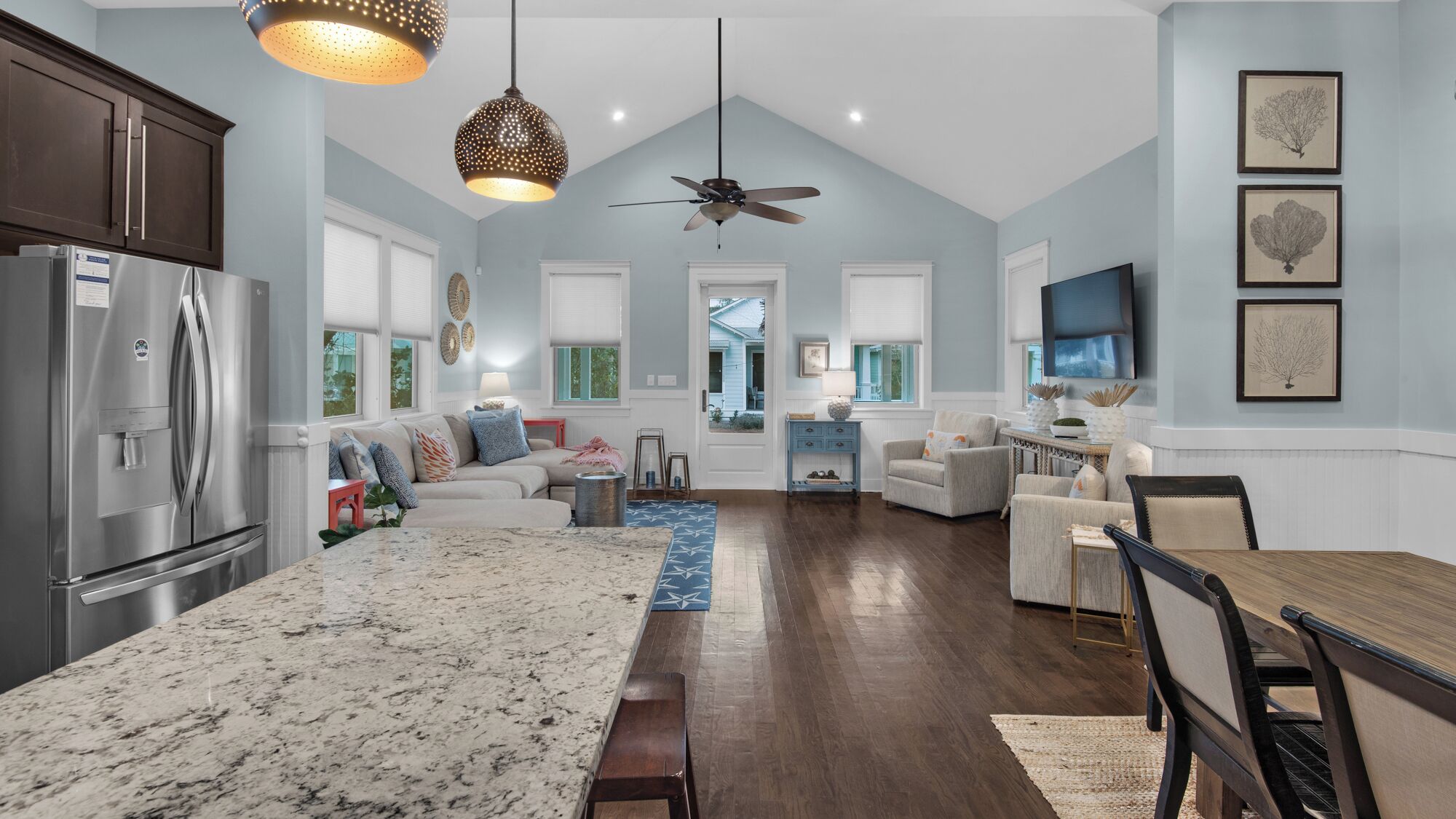 A spacious kitchen with a large island, a dining area with a wooden table, and a living room with a sofa and armchairs.