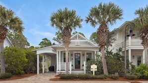 A white colonial-style house with a covered porch, palm trees, and a brick pathway. - Close to Dining & Shopping; 1-floor Cottage; Community Pool (Santa Rosa Beach)