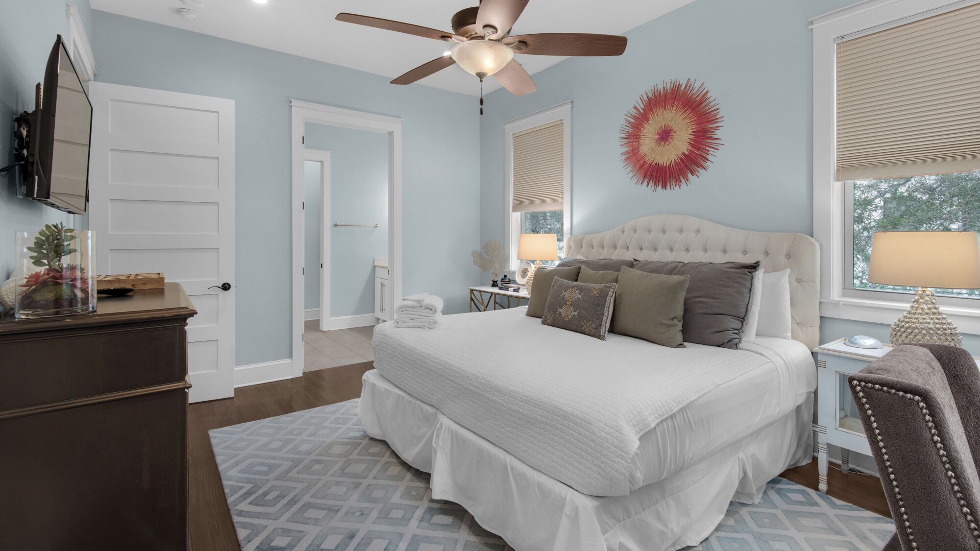 A bedroom with a large bed, a ceiling fan, a TV, and a window with blinds.