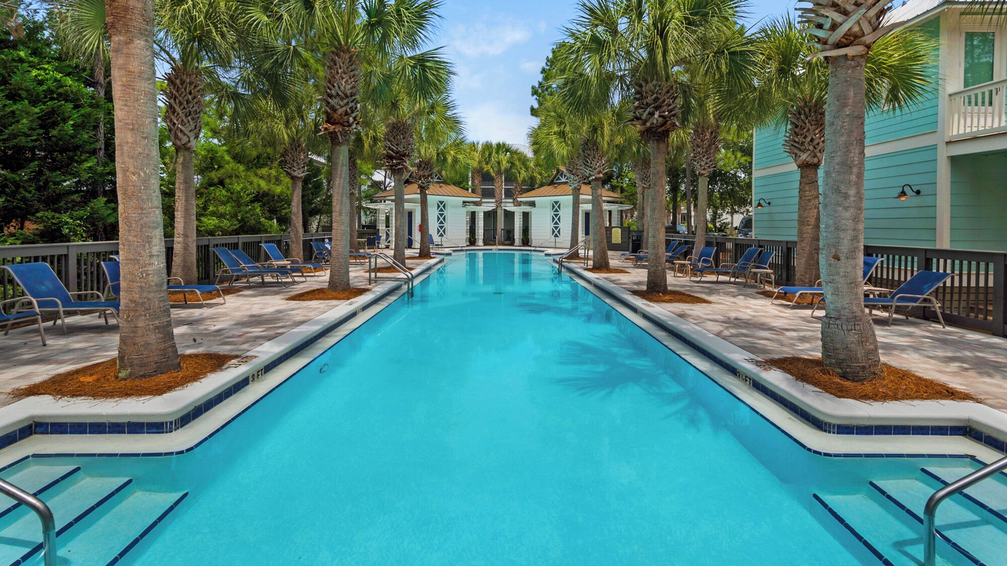 A swimming pool with blue tiles, surrounded by palm trees and lounge chairs.