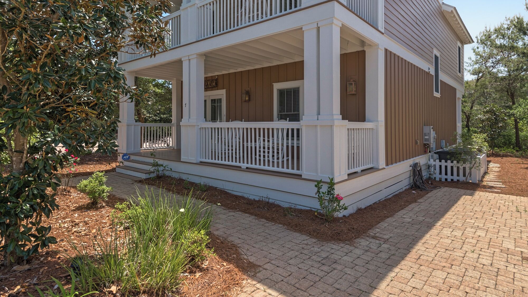 A two-story house with a covered porch, white railings, and a brick pathway leading to the entrance.