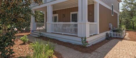 A two-story house with a covered porch, white railings, and a brick pathway leading to the entrance.