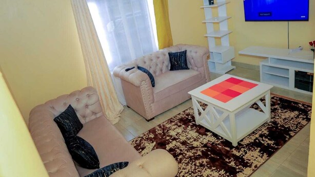 A living room with two sofas, a coffee table, a TV, and a white shelving unit. - Lux Suites Rubi Homes Kisii (Kisii)