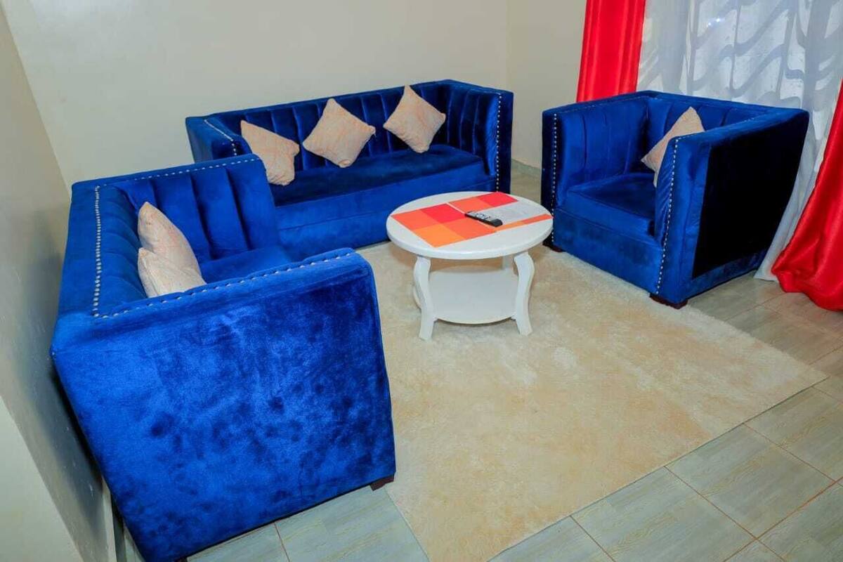 A room with a blue sofa set, a small white table, and red curtains.