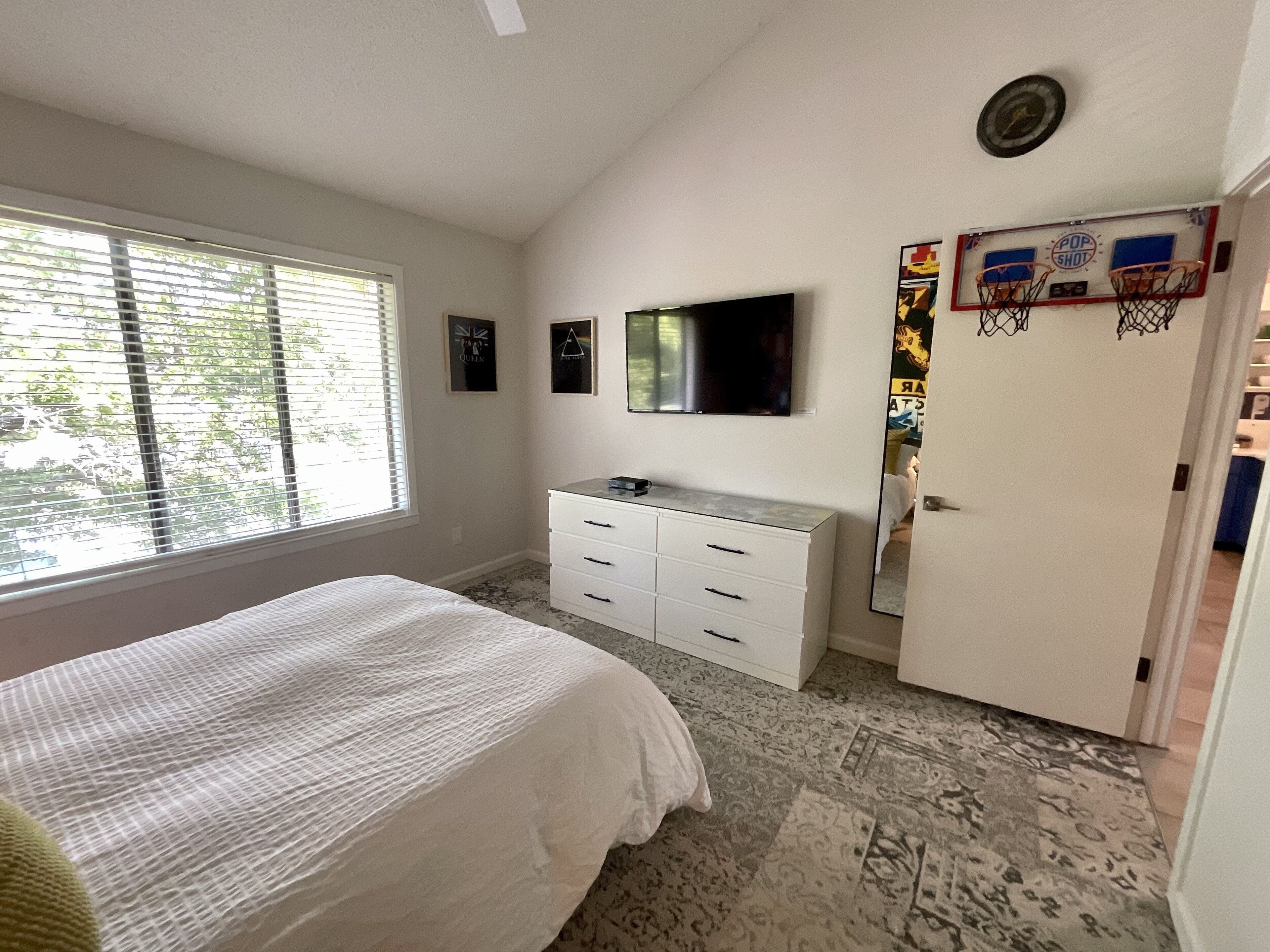 A bedroom with a bed, a dresser, a television, and a door with a poster.