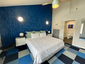 Ein Schlafzimmer mit einem Bett, Nachttischen, einer Kommode und einem durch eine offene Tür einsehbaren Badezimmer.