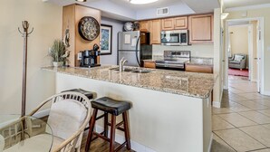 A modern kitchen with granite countertops, stainless steel appliances, and a central island with bar stools. - Carols Coastal K502 3 Bedroom Condo by RedAwning (Rockport)