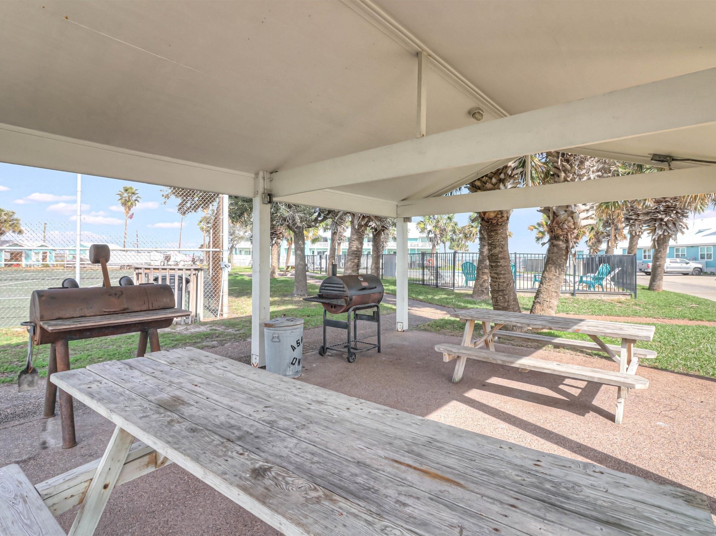 A covered outdoor area with picnic tables and a barbecue grill.