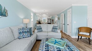 Una sala de estar con un sofá seccional gris, cojines estampados, un sillón de mimbre y una decoración de estrella de mar sobre una bandeja.