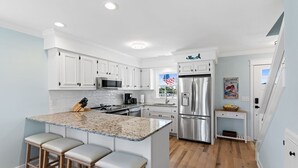 Una cocina moderna con armarios blancos, un refrigerador de acero inoxidable y una encimera de granito.