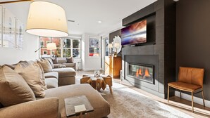 Een moderne woonkamer met een open haard, comfortabele zithoek en een grote televisie aan de muur.