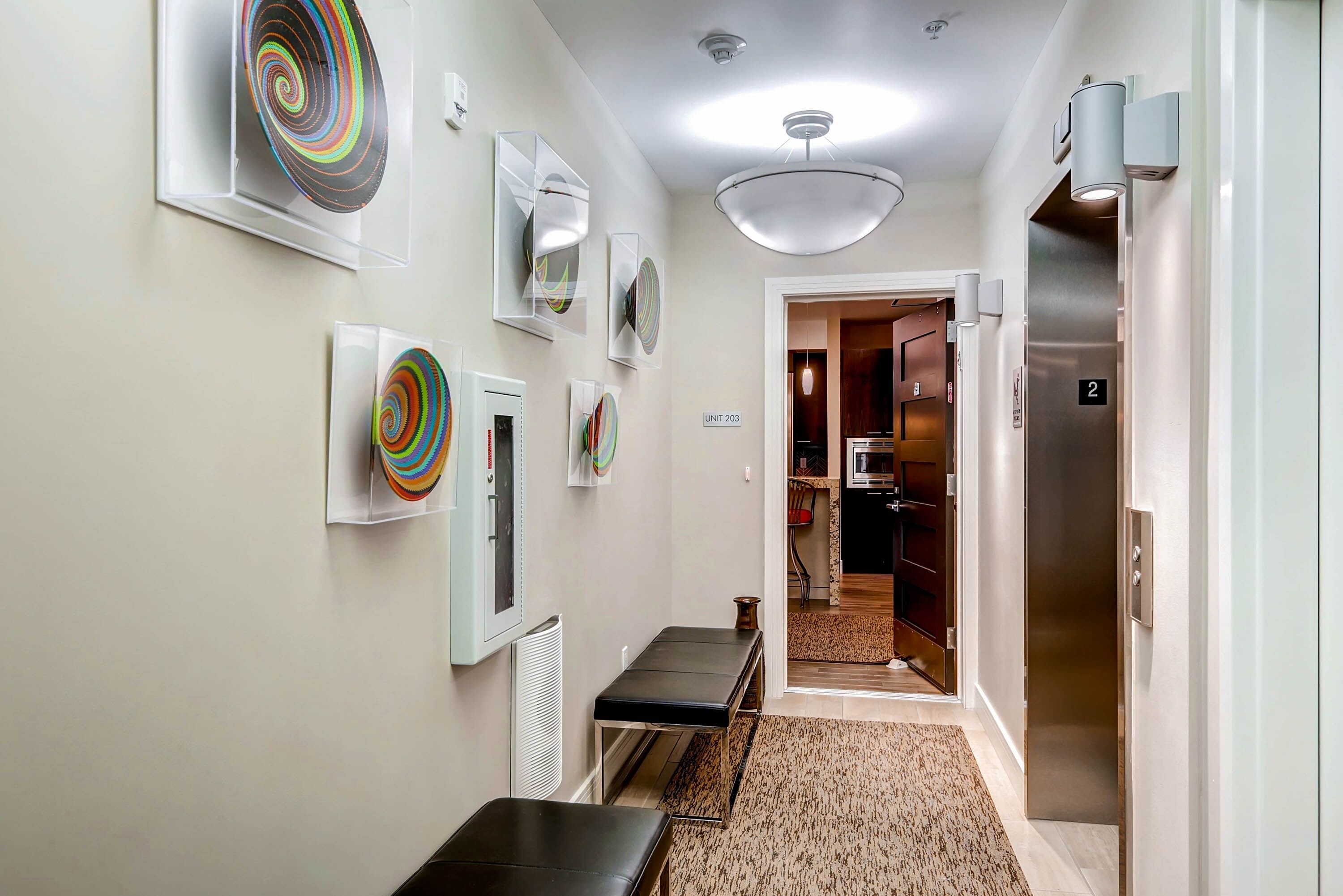 Un couloir avec un banc, un luminaire au plafond et une porte donnant sur un espace cuisine.