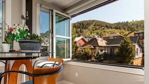 Een balkon met uitzicht op een bebost heuvel, een eettafel met stoelen en een bloempot.