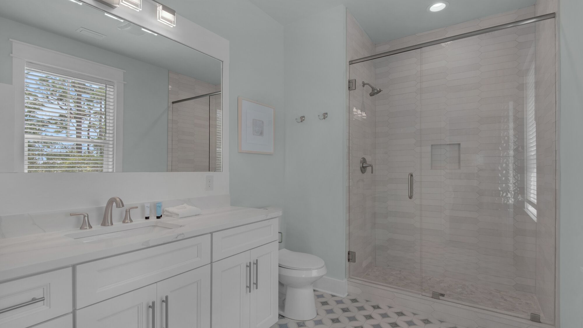 Un baño moderno con ducha envuelta en vidrio, un espejo grande y un lavamanos blanco con tocador.