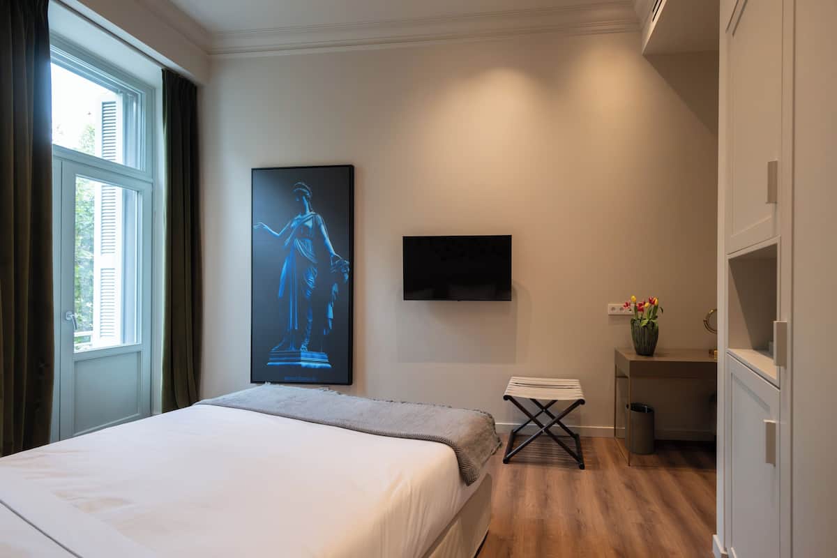 A hotel room with a bed, a desk, a chair, a TV, and a window with curtains.