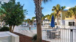 A pool area with a fenced deck, palm trees, and a building with balconies. - Dog Friendly @ Bungalows at Seagrove; 2 Blocks to Beach ~ Overlooks Pool/spa (Santa Rosa Beach)