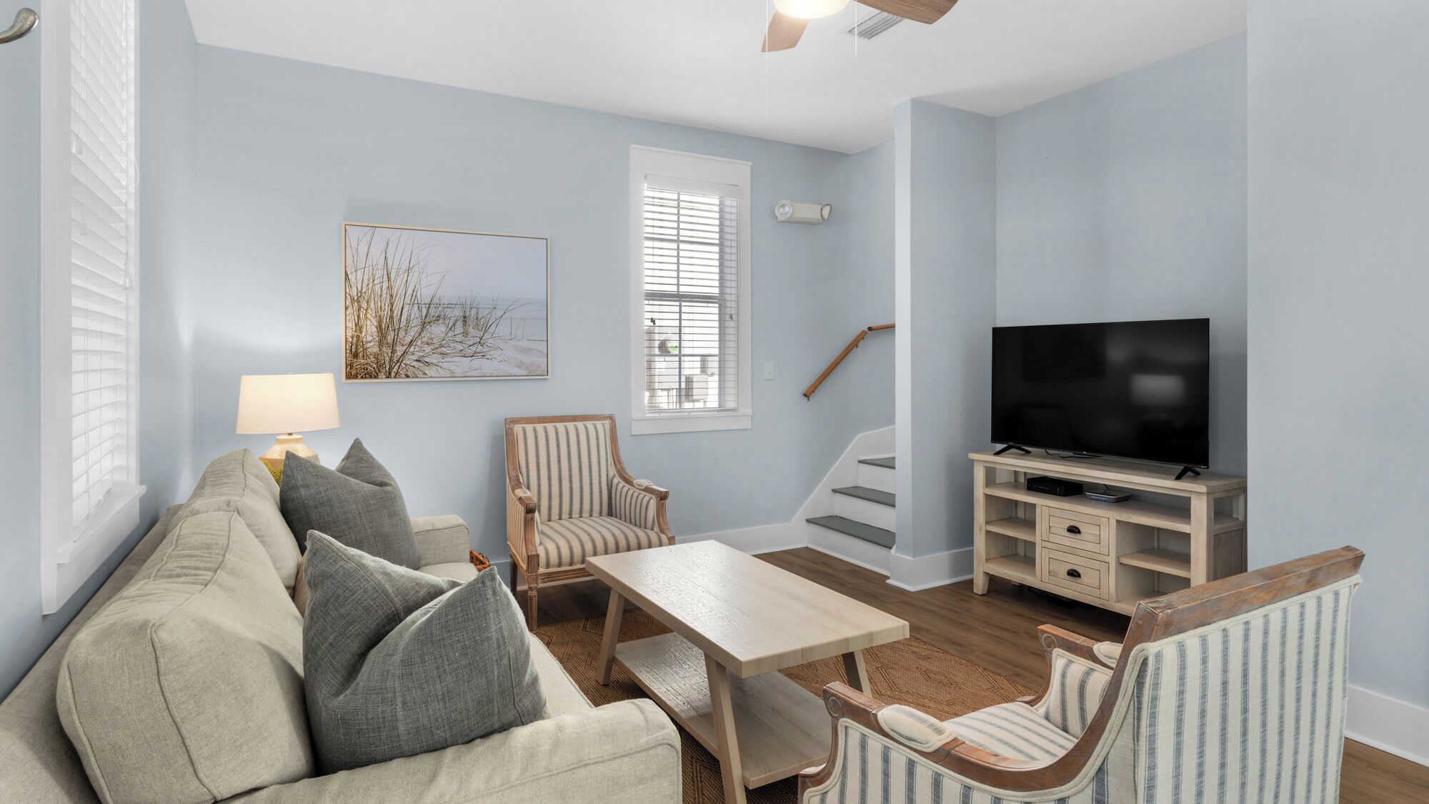 A living room with a sofa, armchairs, a coffee table, a TV stand with a flat-screen TV, and a staircase.