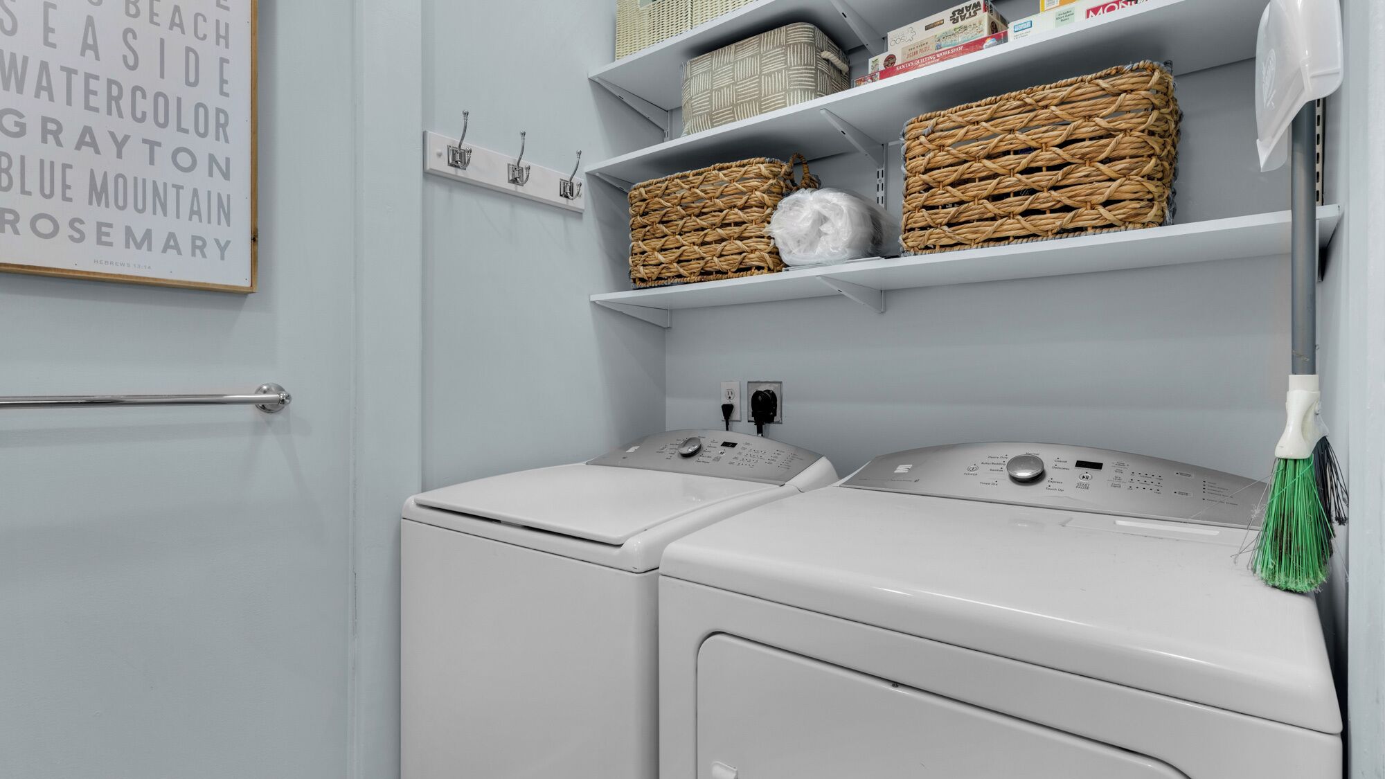 A laundry area with two front-loading washing machines, wicker baskets on shelves, and a wall-mounted towel rack.