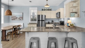A modern kitchen with a central island, stainless steel appliances, and a 'BEACH HOUSE' sign. - Dog Friendly @ Bungalows at Seagrove; 2 Blocks to Beach ~ Overlooks Pool/spa (Santa Rosa Beach)