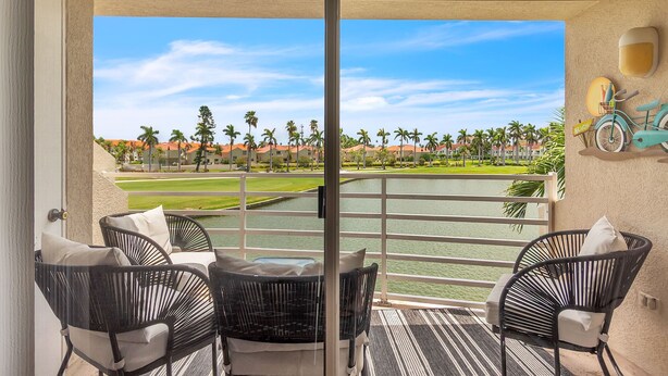 A balcony with wicker chairs and a view of a golf course and water body.