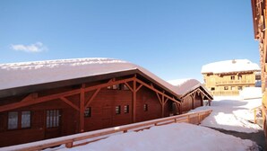 Ein mit Schnee bedecktes Holzgebäude mit geneigtem Dach, wahrscheinlich ein Hotel oder eine Lodge, mit blauem Himmel im Hintergrund.