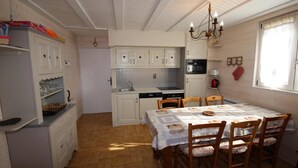 Eine kompakte Küche mit weißen Schränken, einem Esstisch mit Stühlen, einer Pendelleuchte und einem Fenster mit Vorhängen.