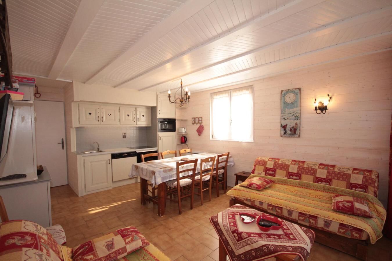 A cozy, well-lit room with a dining table, chairs, a sofa, and a kitchen area with cabinets and appliances.